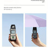 A hand holds a black electronic device measuring UV intensity under direct sunlight.