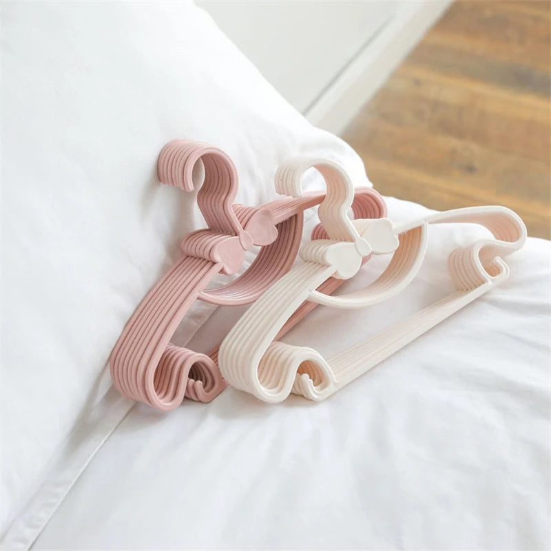 Pink and white plastic clothes hangers for kids and coats displayed on a white bedsheet.