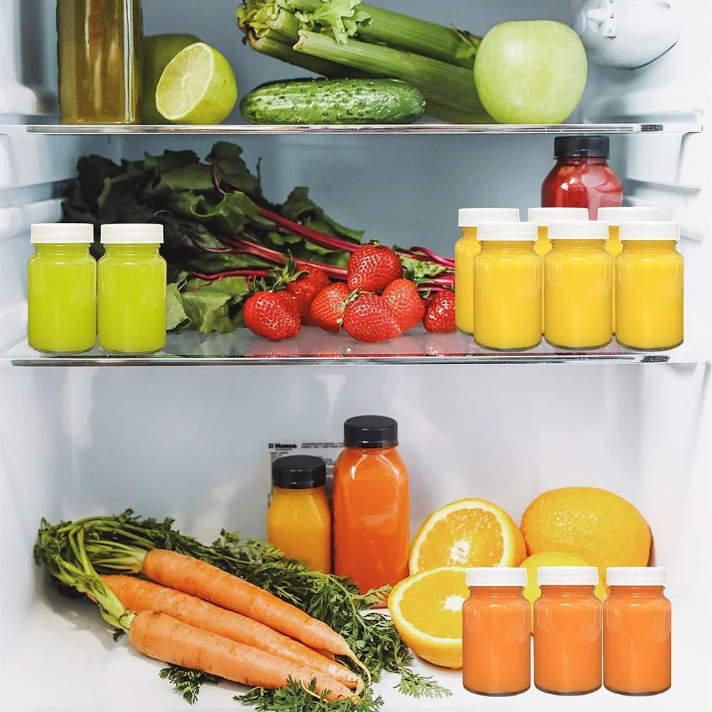 A refrigerator shelf displaying various glass juice bottles filled with green, yellow, and orange juices and fresh vegetables