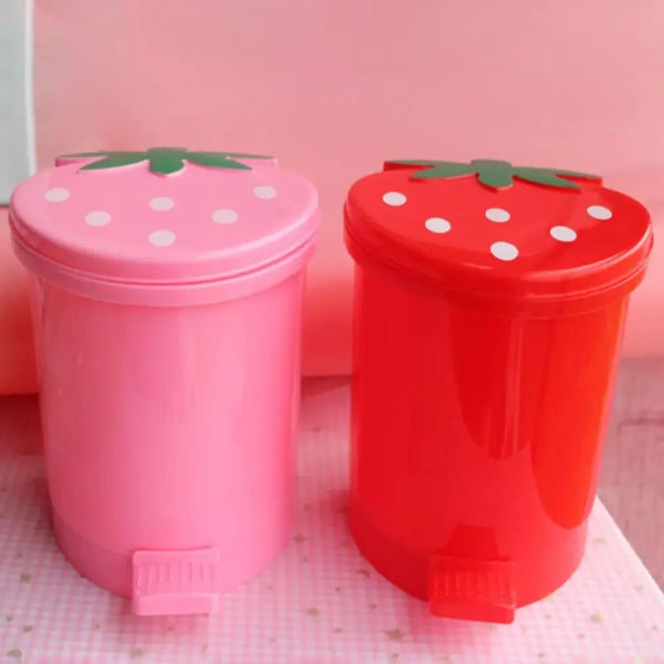 Pink and red reusable decorative strawberry pop-up trash cans sitting on a pink surface.