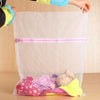 A clear mesh laundry bag filled with pink and yellow clothing, being held by a person.