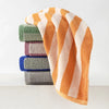 A stack of plaid cotton bath towels in shades of orange, green, purple, and blue.