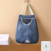 A dark blue mesh garbage bag storage organizer hanging on a wall with light blue straps.