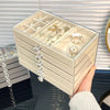 A clear acrylic 5-tier desktop jewelry organizer rack filled with various rings and jewelry, held by a hand.