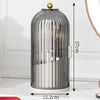 A cylindrical glass organizer for makeup brushes with a gold lid and white base.