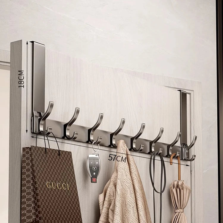 A silver over-the-door organizer rack with extended arms is mounted on a white wall, holding various hangers and bags.