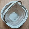 A white collapsible water bucket with a handle is shown on a wooden surface.