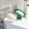 An oval clear plastic soap dish with drainage holes holding a pale green bar of soap on a white countertop.