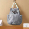 A gray mesh garbage bag storage organizer hangs on a wall, featuring a handle and multiple compartments.