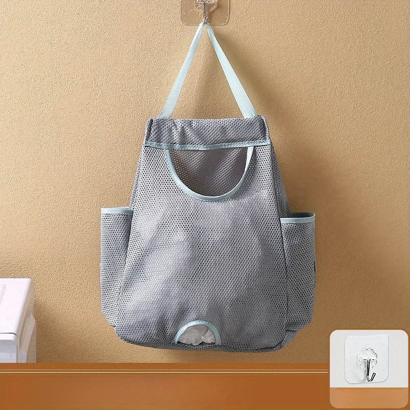 A gray mesh garbage bag storage organizer hangs on a wall, featuring a handle and multiple compartments.