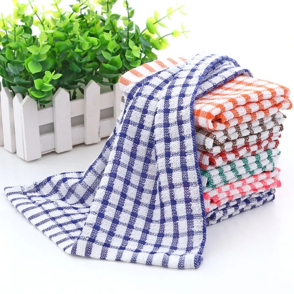 A stack of six absorbent cotton kitchen tea towels in various plaid patterns, displayed next to a potted green plant.