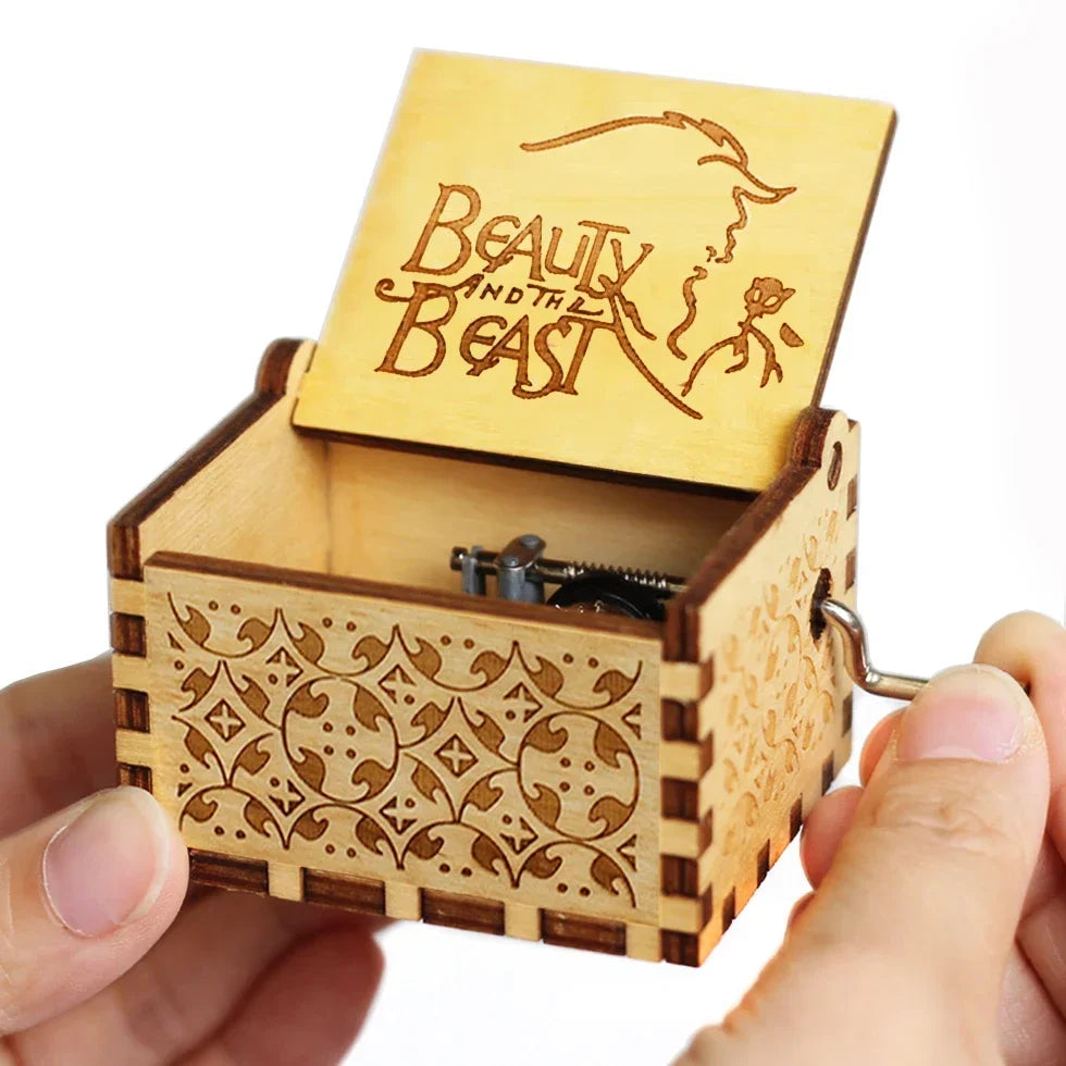 An antique wooden hand crank music box with a lid featuring the text Beauty and the Beast is held in a hand.