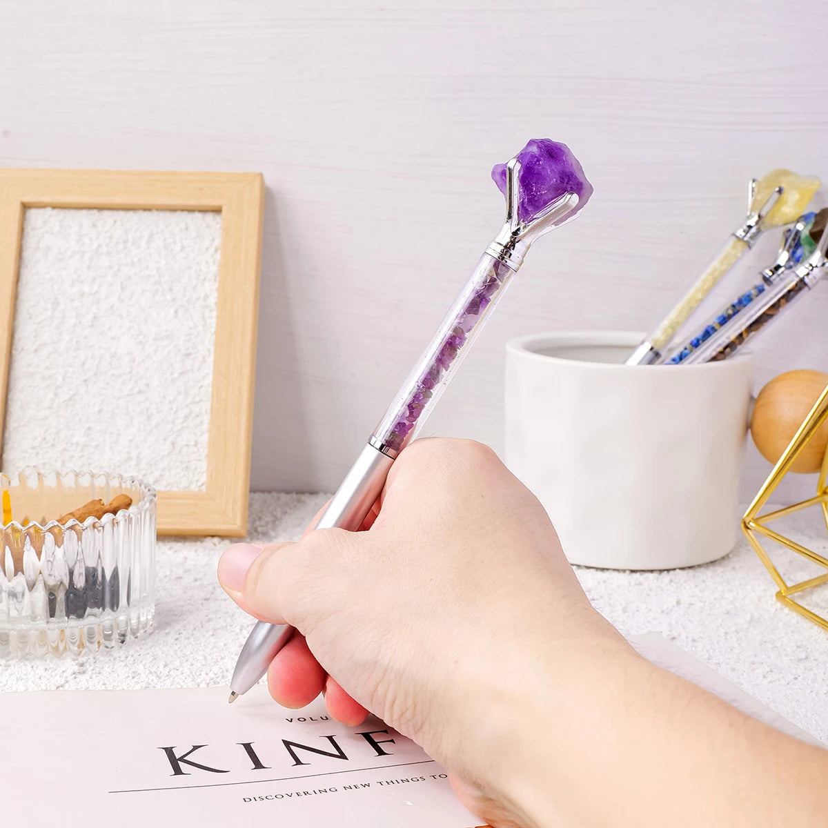 A hand holds a silver pen with a purple amethyst crystal tip resting on a paper.