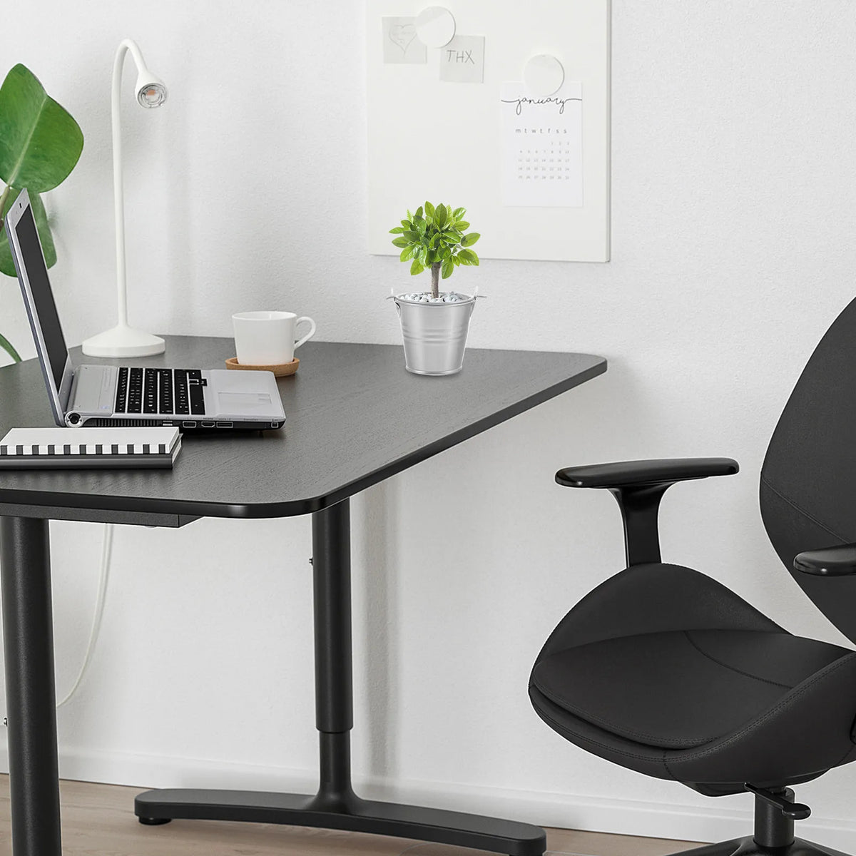 A vintage iron flower bucket used as home decor sits on a dark desk next to a laptop and a potted plant.