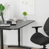 A vintage iron flower bucket used as home decor sits on a dark desk next to a laptop and a potted plant.
