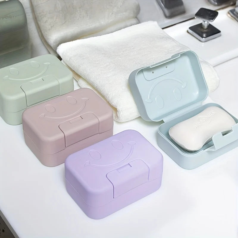 A set of aesthetic ceramic soap dishes with lids in pastel colors resting on a white surface next to a white towel.