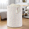 A large woven storage hamper in a light pink and cream striped pattern with tassels, sitting on a wooden floor.