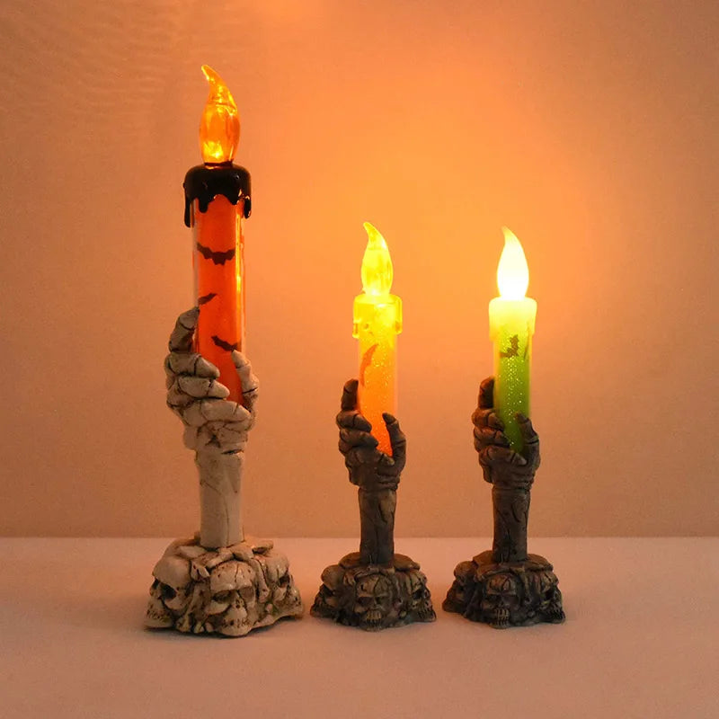 Three skeleton hand shaped LED candles glowing orange, yellow, and green against a warm background.