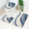 A set of three soft non-slip bathroom rugs featuring gray and blue striped patterns placed near a white toilet.