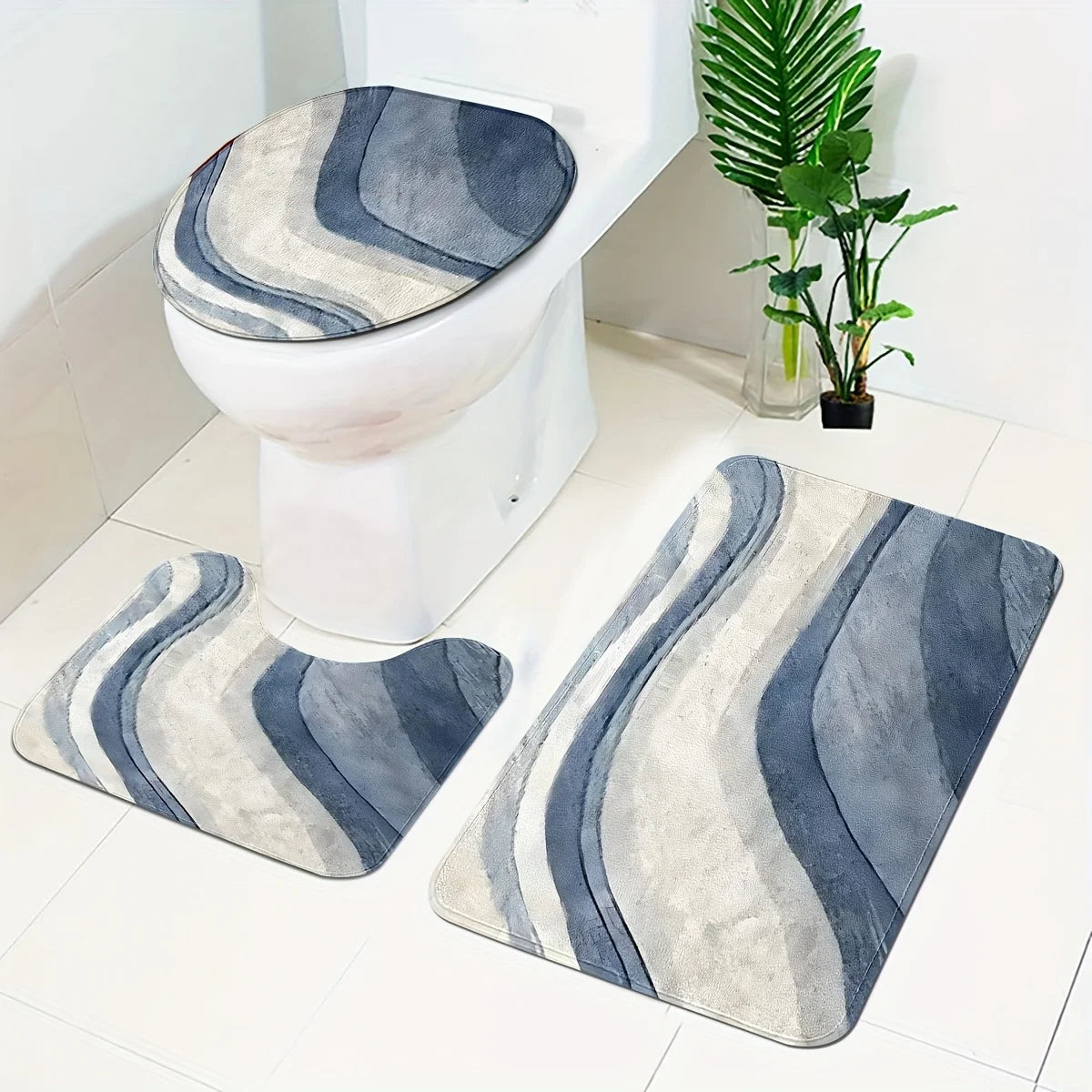 A set of three soft non-slip bathroom rugs featuring gray and blue striped patterns placed near a white toilet.