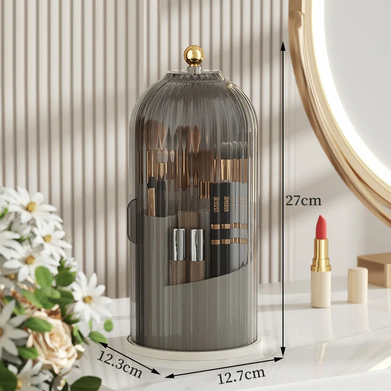 Hoher zylindrischer Glas-Kosmetikorganizer mit goldener Klappe und mehreren Pinselhaltern auf weißem Untergrund.