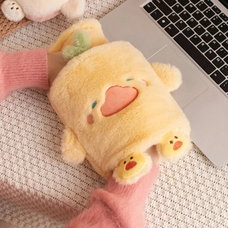 A yellow plush animal hot water bottle is resting on a white laptop keyboard and pink knitted fabric.