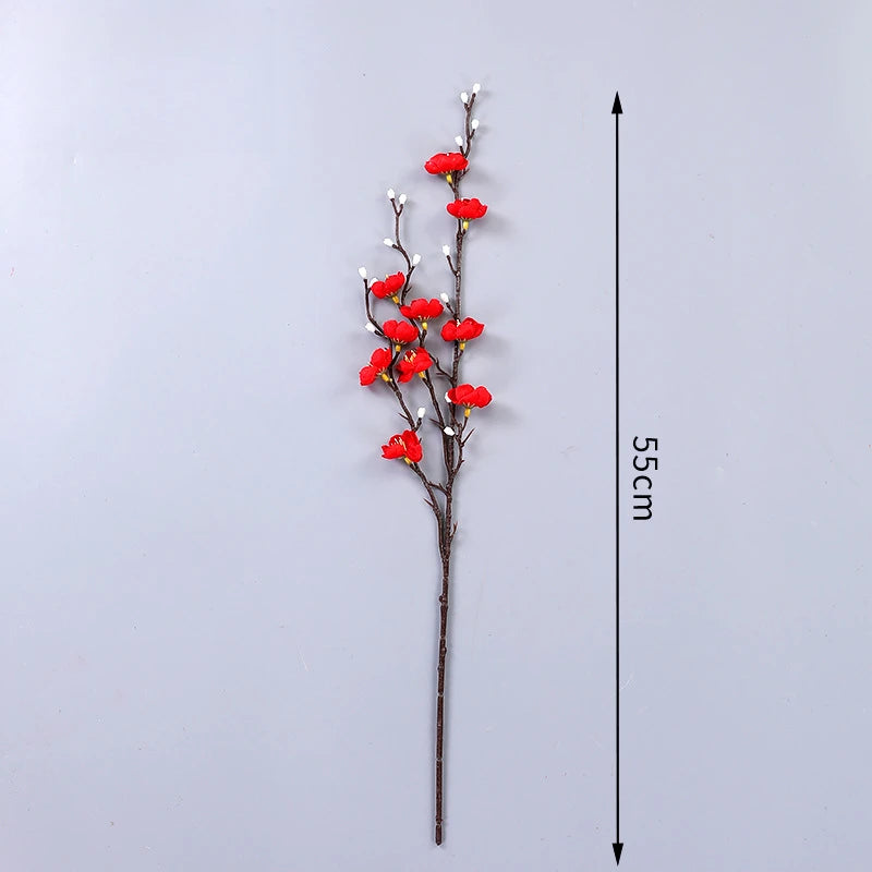Eine schlanke Zweig aus künstlichen roten Pflaumenblüten mit weißen Knospen, dargestellt vor weißem Hintergrund und Maßstab.