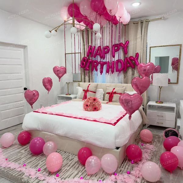 A pink heart birthday balloon set decorated with pink confetti and balloons on a bed.