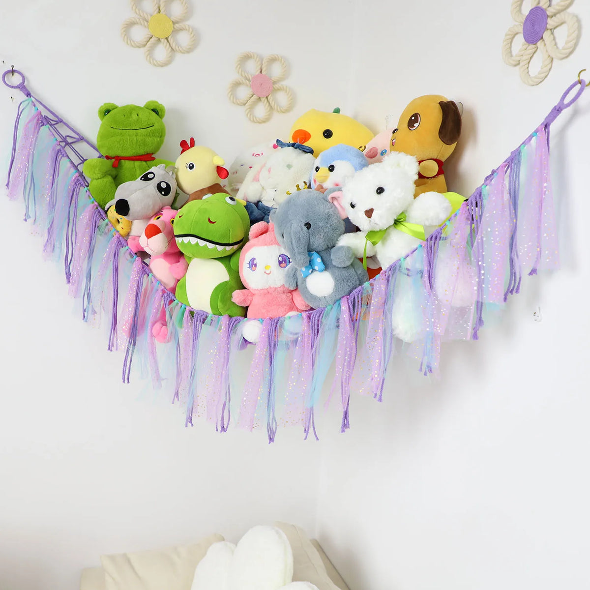A bohemian stuffed animal hammock featuring various plush toys hanging from a purple and pink fabric streamer.