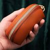 A hand holds an orange leather key organizer wallet with a visible zipper closure.
