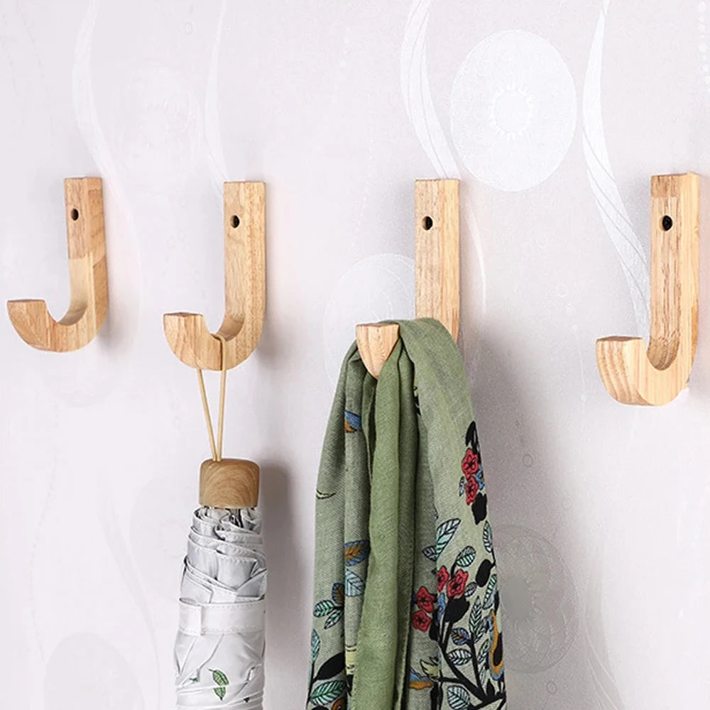 Natural oak wood wall hooks with screws hanging on a white wall next to a green fabric.