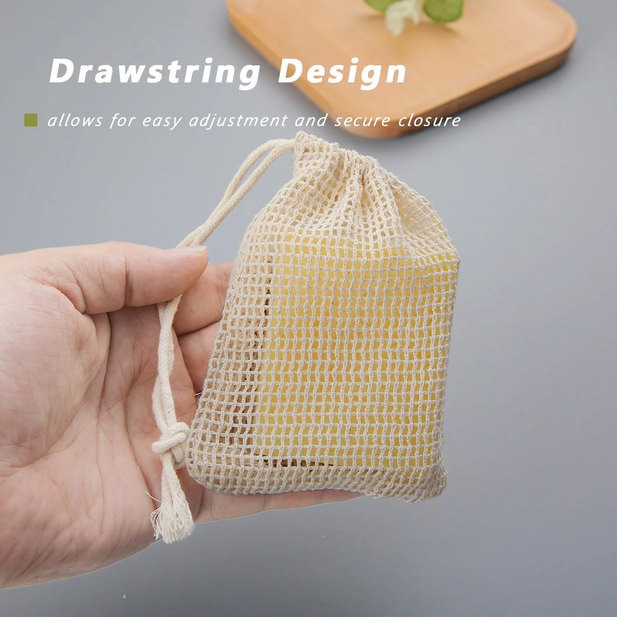 A hand holds a natural cotton mesh soap saver pouch, demonstrating its drawstring design for easy closure.
