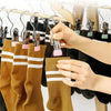 A hand is hanging a mustard yellow knitted sock onto a wooden hanger using a stainless steel clothespin set.