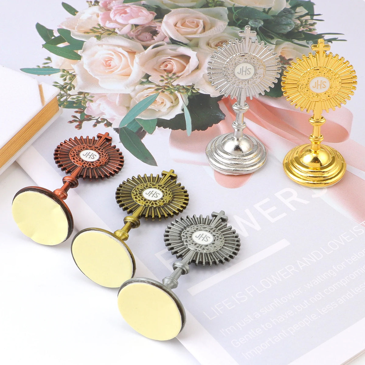 A collection of mini metal religious ornaments featuring floral designs and the initials JHS, displayed on a white background