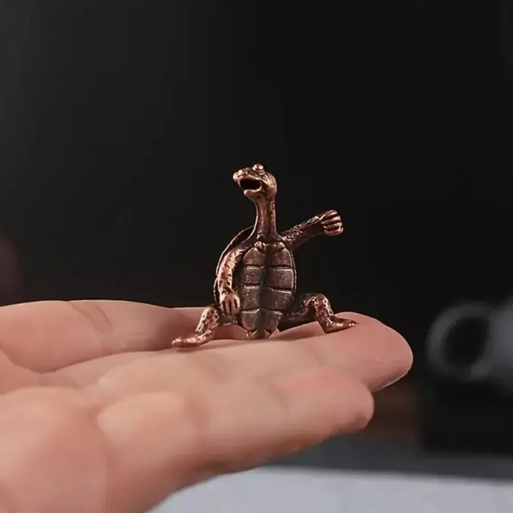 Une petite tortue en métal texturé est tenue dans la main d'une personne sur un fond sombre.