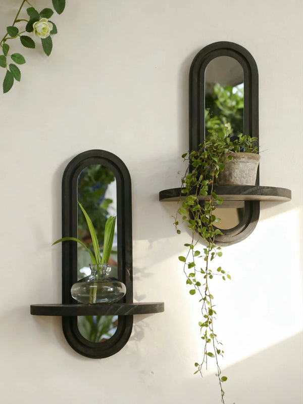 A modern geometric wall shelf with a mirror holds a glass vase and trails of green ivy against a white wall.