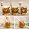 A set of glass honey jars with wooden dippers and natural honey on a woven mat.