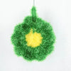 A green, fuzzy Christmas ornament shaped like a wreath with a yellow center.