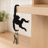 A black monkey silhouette hangs from a wooden key hanger decoration on a light wood shelf.
