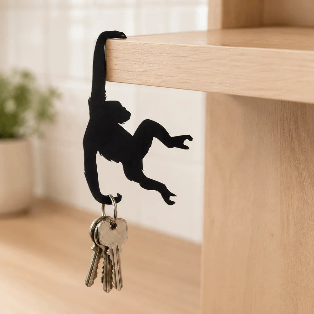 A black monkey silhouette hangs from a wooden key hanger decoration on a light wood shelf.