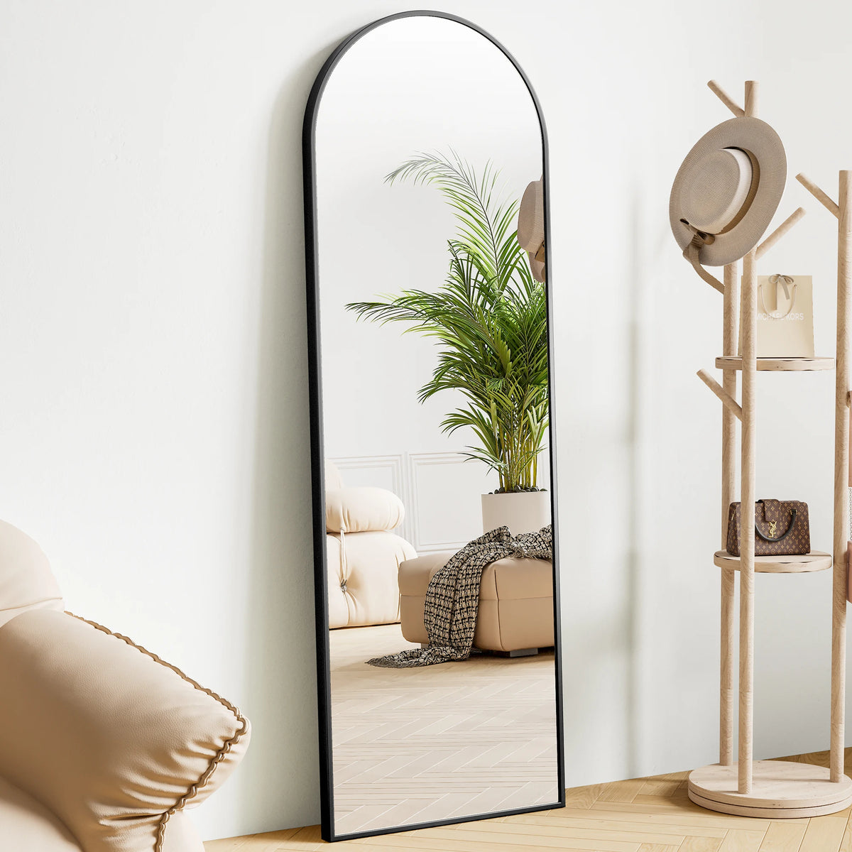 A full body standing wall mirror with an arched top reflects a potted palm plant and interior decor.