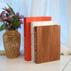 A stack of three decorative fake books in orange, white, and wood tones displayed on a white surface.