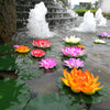 Colorful artificial lotus flowers floating on water with a backdrop of a tiered stone waterfall