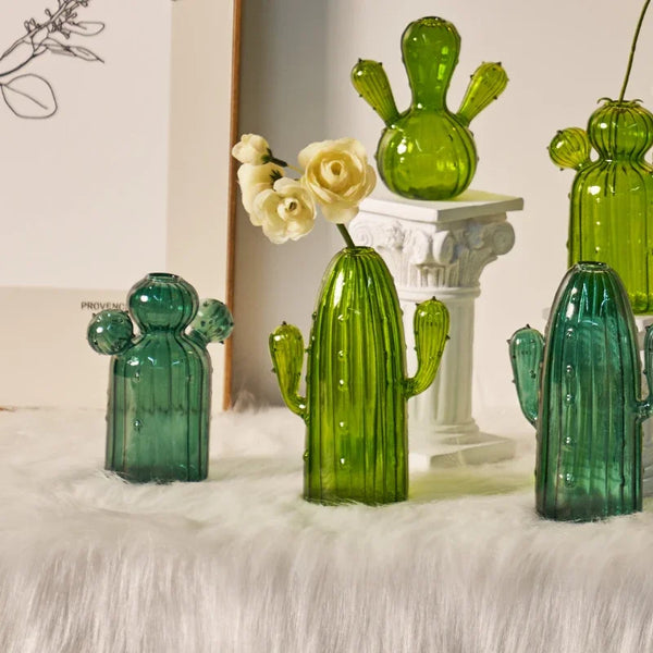 Collection de vases en cactus de verre vert vif, exposés sur un piédestal blanc.