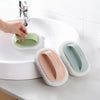 A hand is using a magic sponge scrubber with an ergonomic handle to clean a white sink basin.