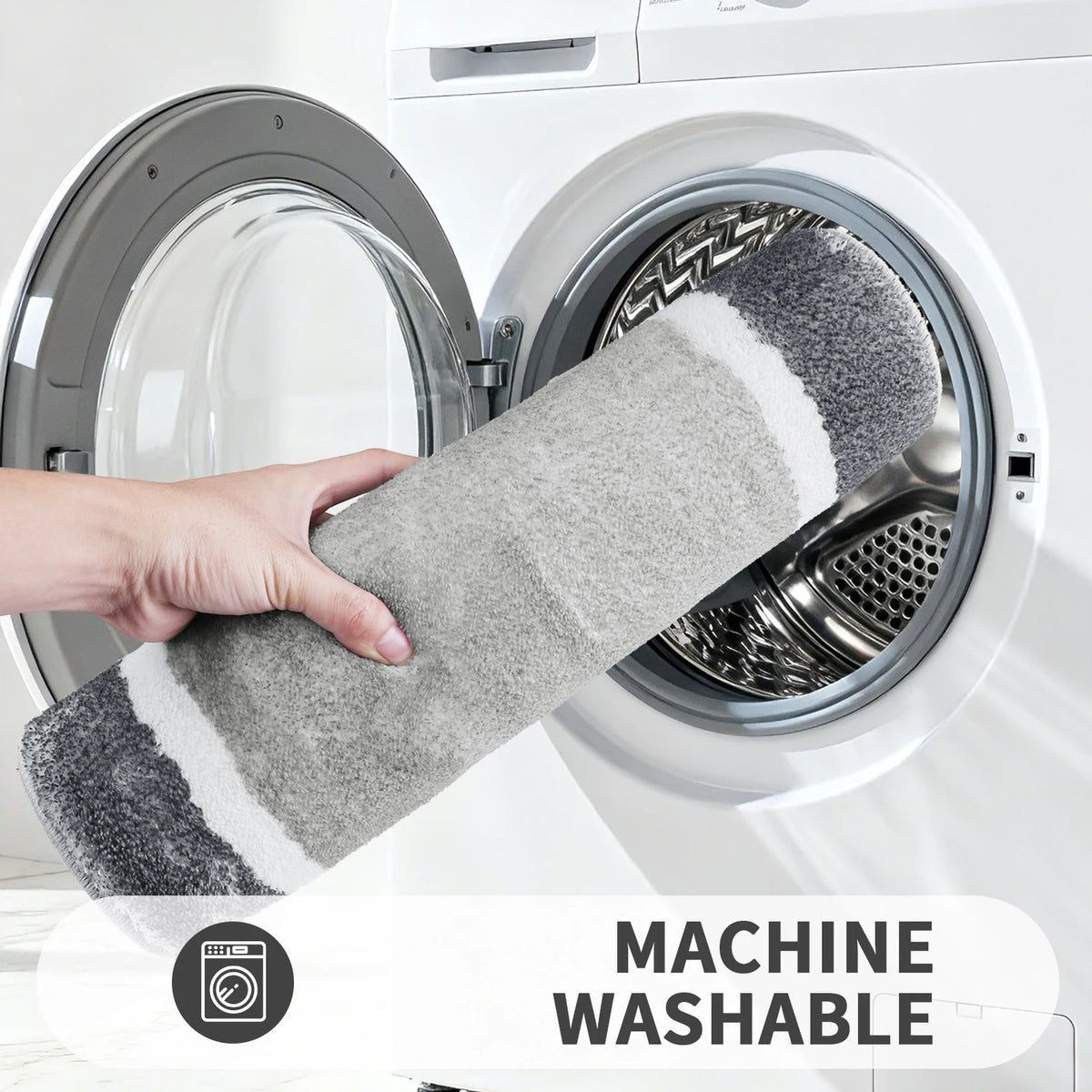 A hand is holding a gray and white memory foam bathroom rug inside a white washing machine drum.