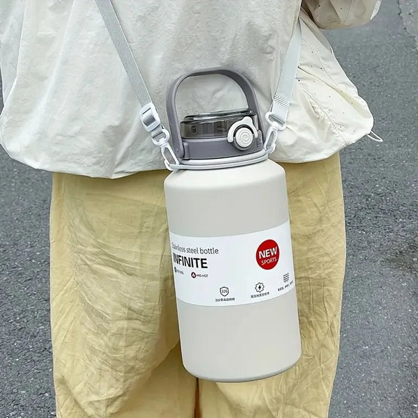 A white stainless steel insulated tumbler with a handle and straw is being held by a person wearing light-colored pants.