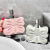 A pink ceramic pump dispenser bottle with a bowknot design is shown next to a white one on a marble surface.
