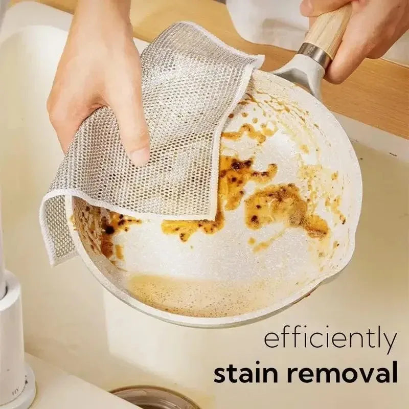Hands are using a mesh cleaning cloth to remove stains from a round, light-colored cooking pan.