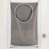 A gray fabric laundry organizer with a circular opening hanging on a white door.